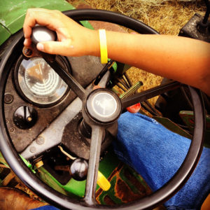 Kid driving a tractor with yellow bracelet and blue jeans